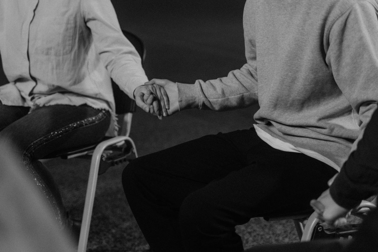 Home Black and white image of people holding hands in a group therapy session enhancing mutual support.