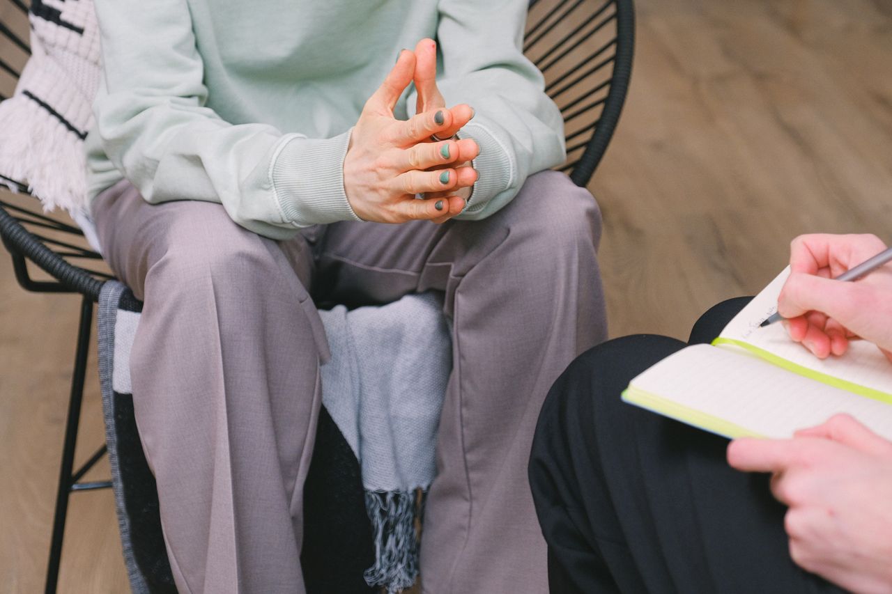 Home Crop unrecognizable psychotherapist taking notes in journal while interacting with woman on chair during psychological counseling indoors